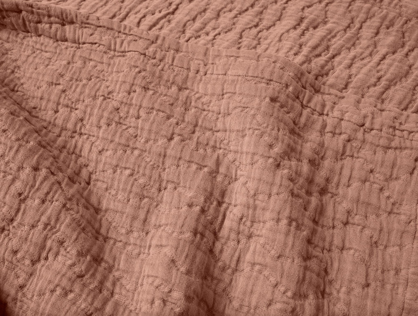 Close-up of Coyuchi Pescadero Matelassé blanket in terracotta, showing textured wave quilting.