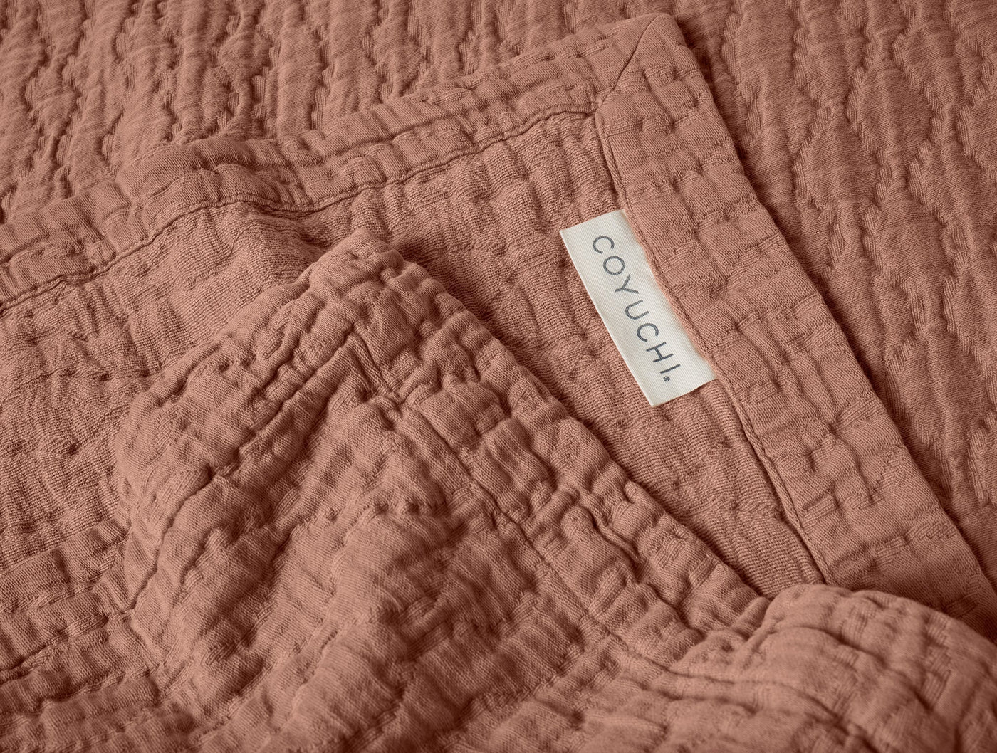 Close-up of Coyuchi label on terracotta matelassé blanket corner, showing textured weave detail.