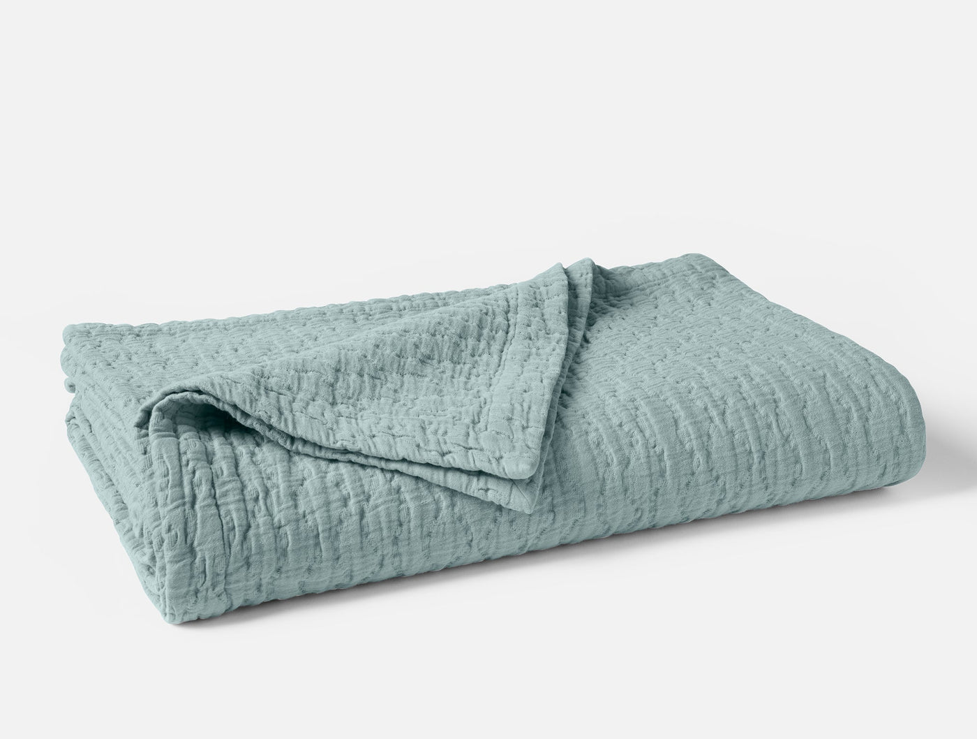 Coyuchi Pescadero Matelassé blanket folded, seafoam blue with textured wave pattern.