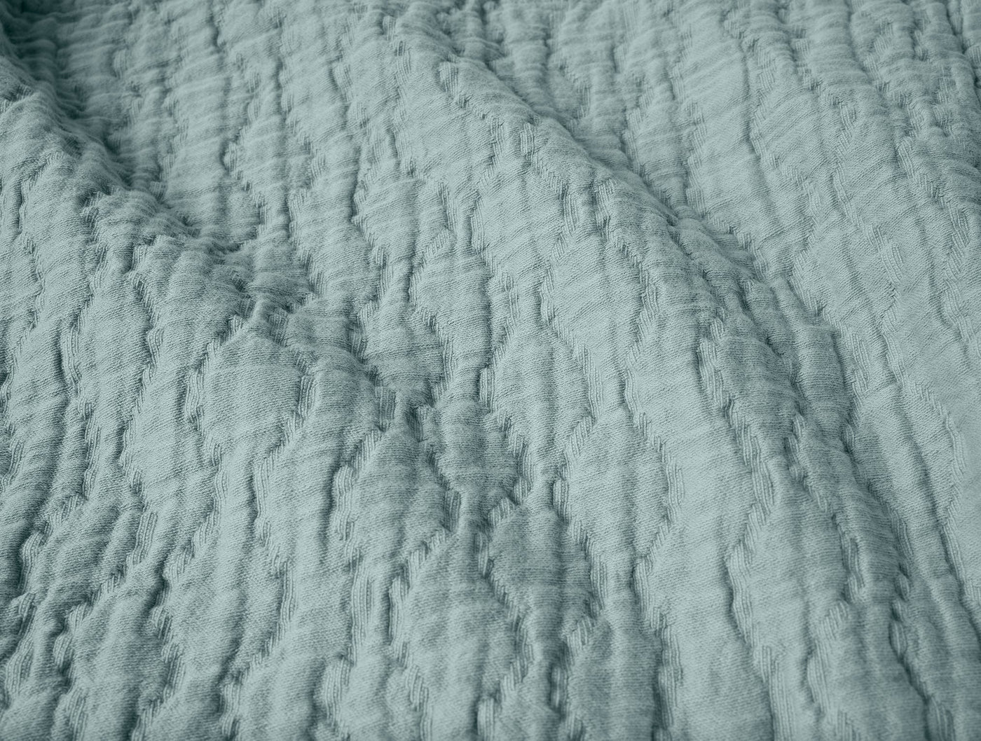 Close-up of Coyuchi Pescadero matelasse blanket in sage blue with quilted wave texture.