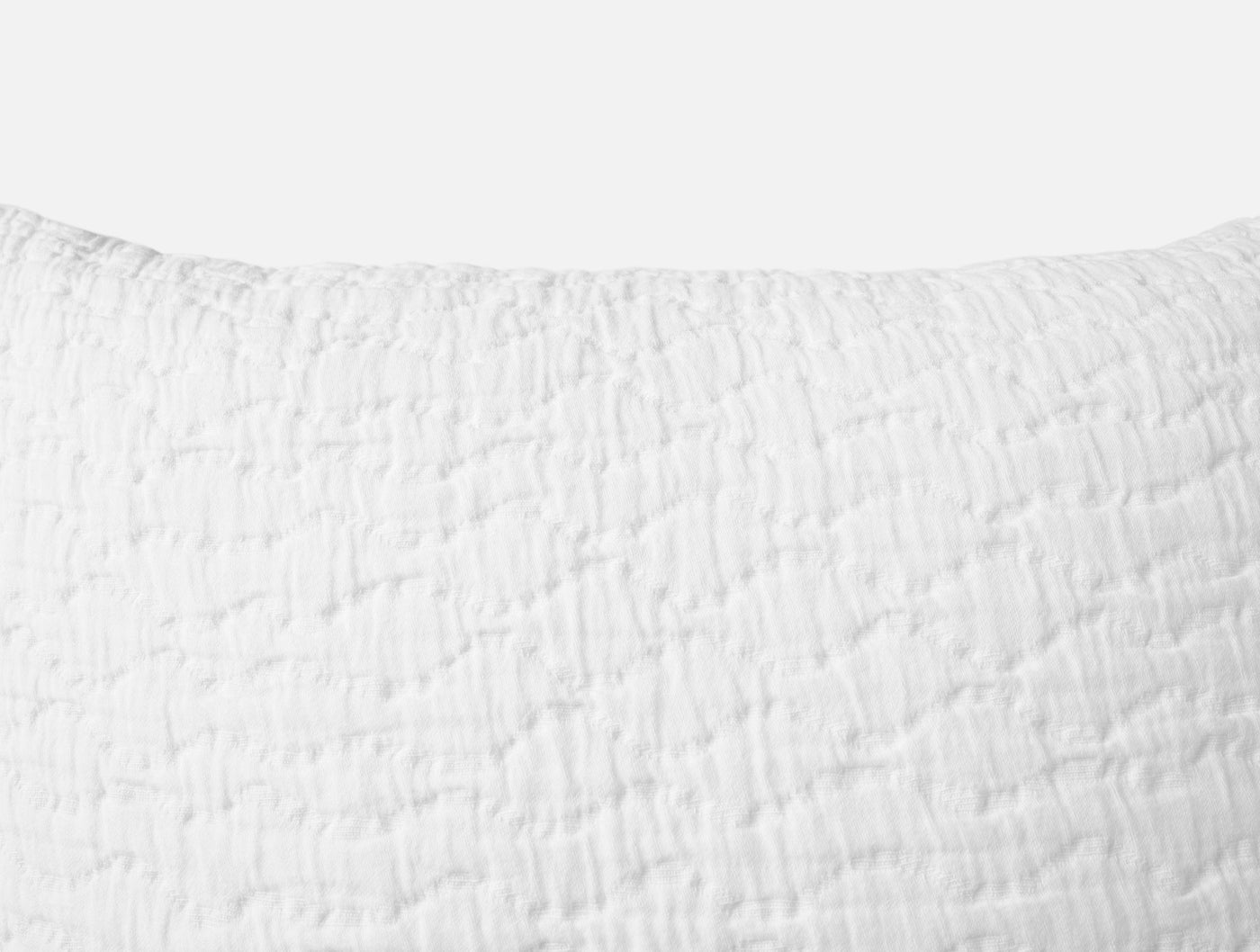 Close-up of white matelassé texture on Coyuchi Pescadero pillow sham, showing quilted wave pattern.