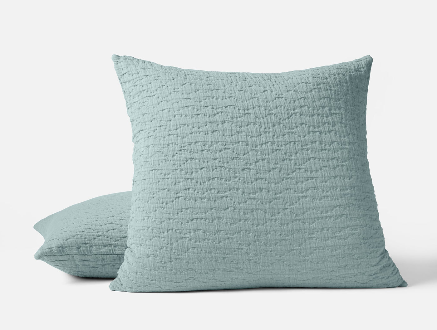 Seafoam matelassé pillow shams stacked, showing quilted linen texture.