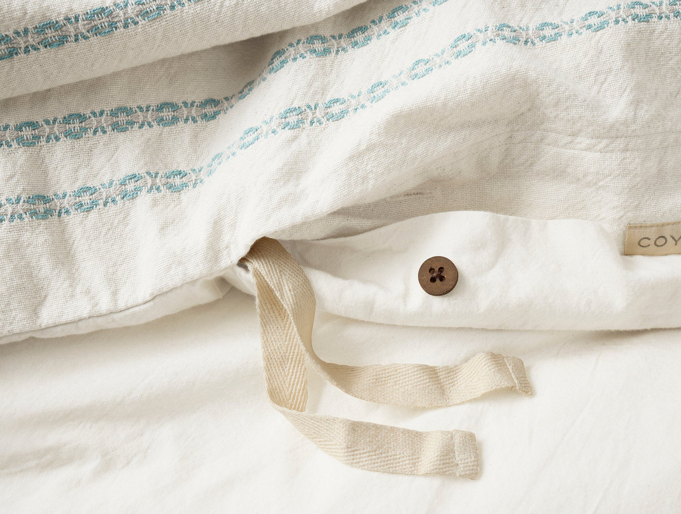 Close-up of Coyuchi duvet cover interior corner with natural cotton tie and dark button closure.