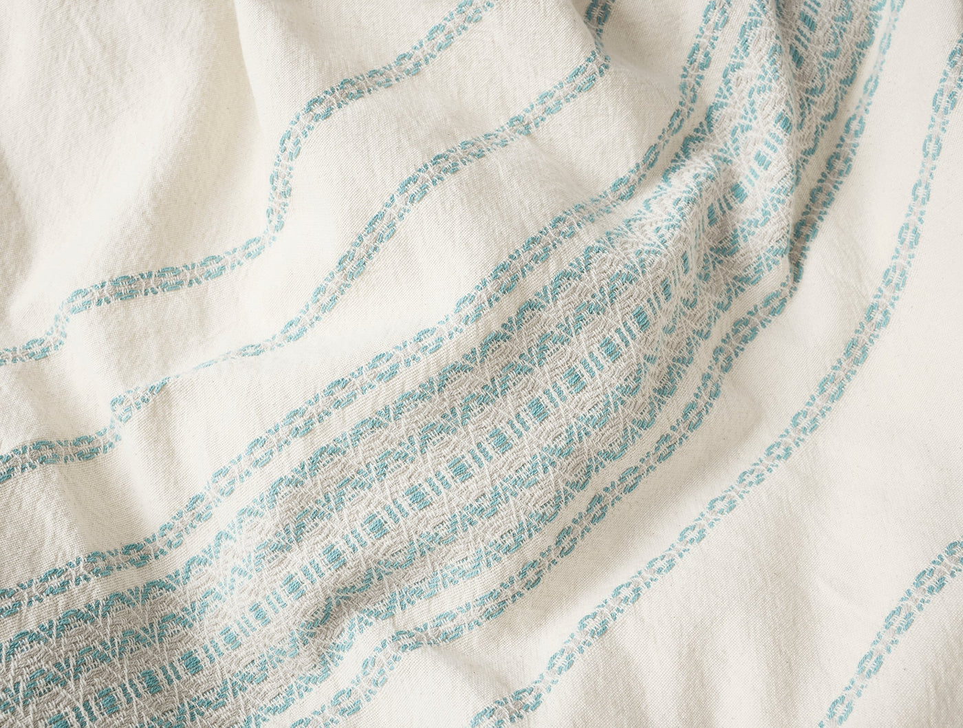 Close-up of ivory Coyuchi Rippled Stripe duvet cover showing aqua woven stripe detail.