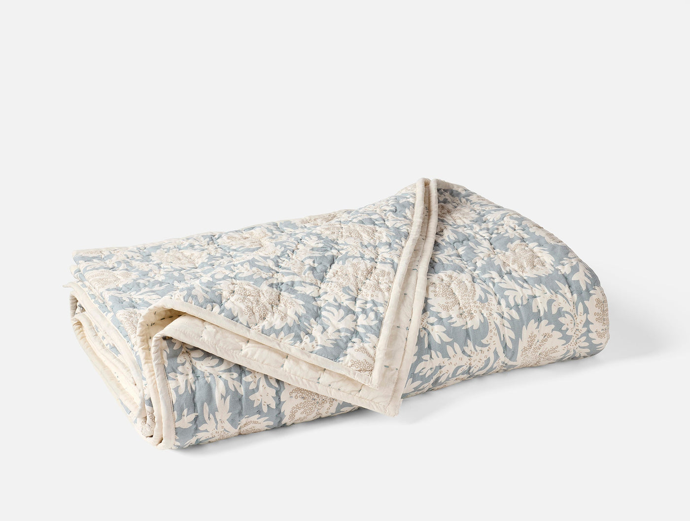 Folded Coyuchi Robles quilt showing dusty blue floral block-print pattern and ivory scalloped trim.