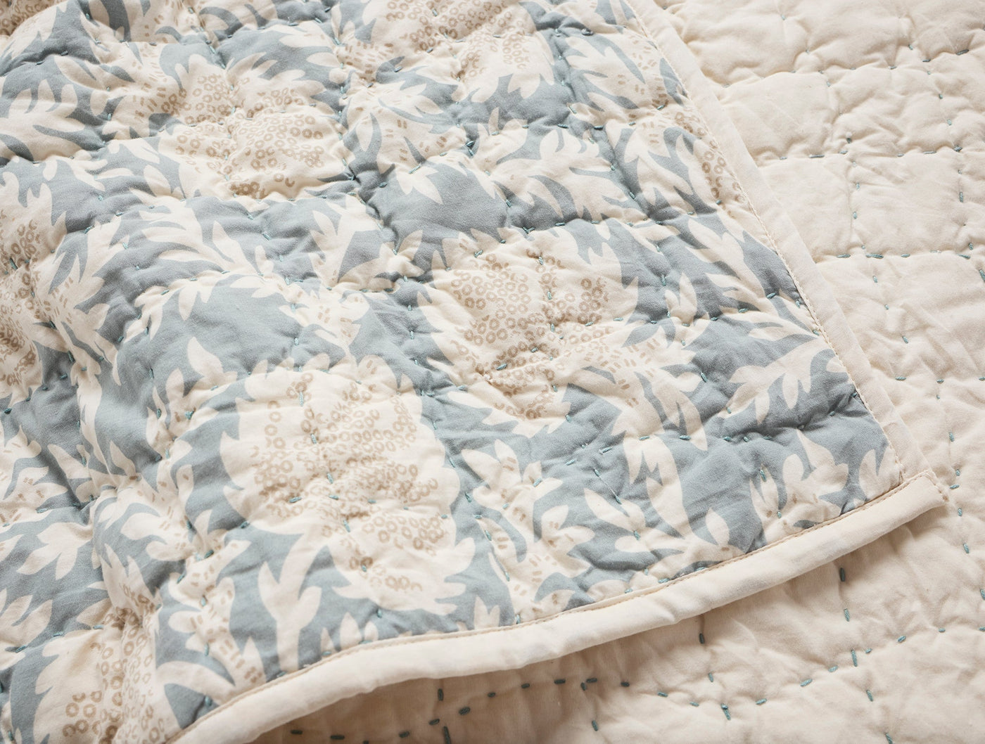 Close-up of Coyuchi Robles quilt corner, showing dusty blue floral print and ivory quilted stitching.