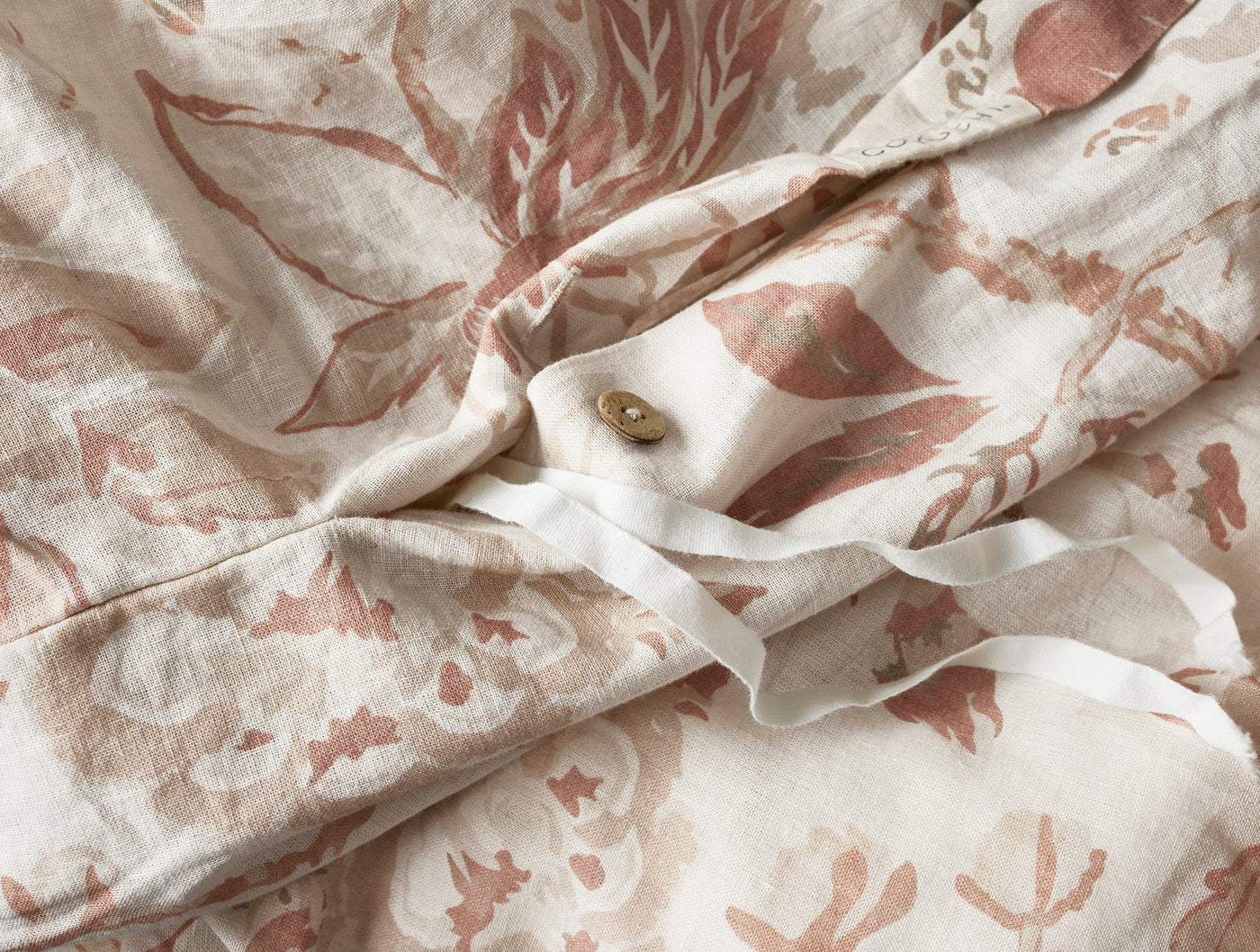 Close-up of ivory linen duvet cover with dusty rose botanical print and button closure detail.