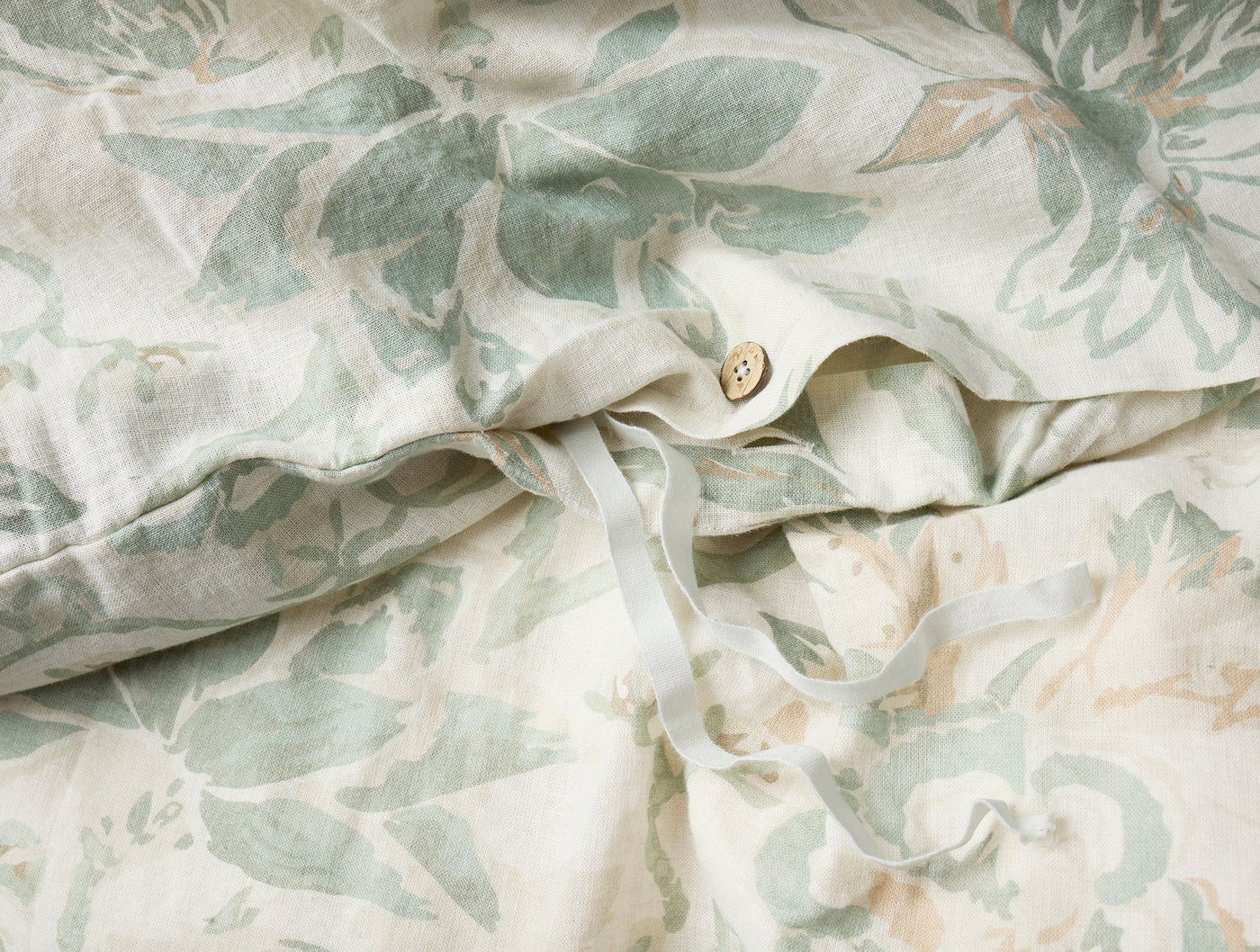 Close-up of button closure on Coyuchi Sea Bloom duvet cover with sage floral print.