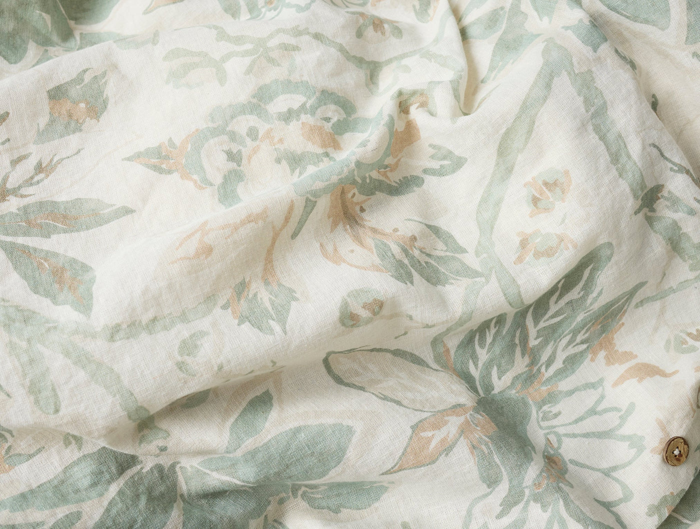 Close-up of Coyuchi Sea Bloom duvet cover in sage and ivory floral linen, button detail visible.