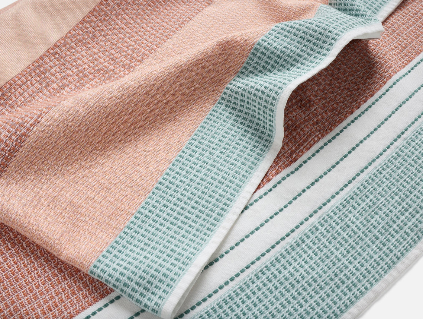 Close-up of Coyuchi Seabright beach towel showing coral and sage waffle-weave texture with stripe border.