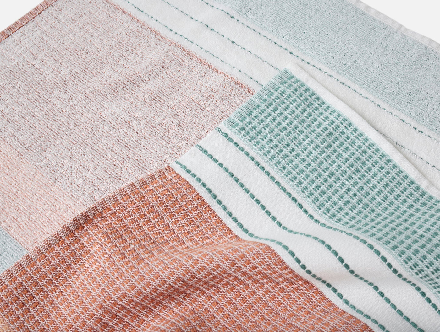 Close-up of Coyuchi Seabright beach towel showing coral, blush, and seafoam woven grid panels.