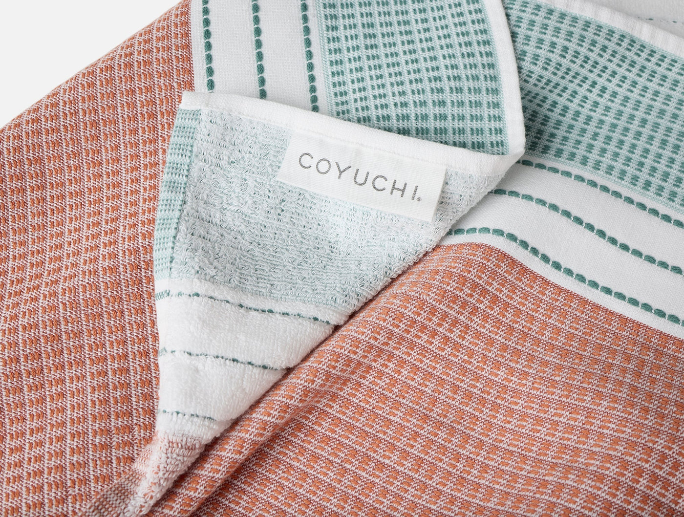 Coyuchi label detail on folded terracotta and sage striped beach towel.
