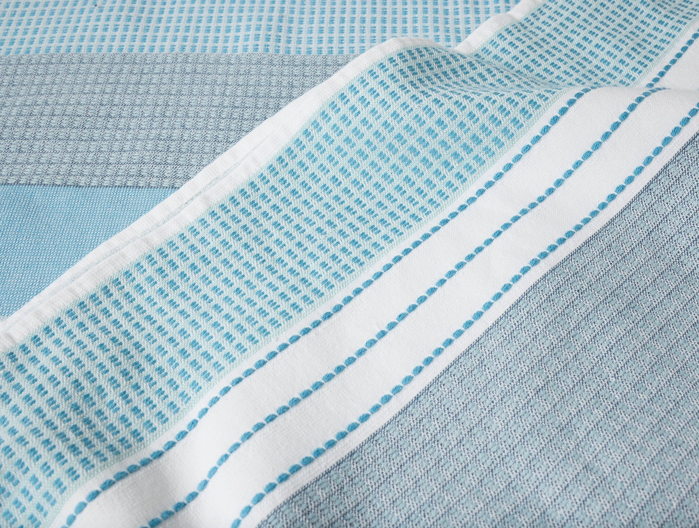 Close-up of Coyuchi Seabright beach towel hem with teal dotted stripe on white border.