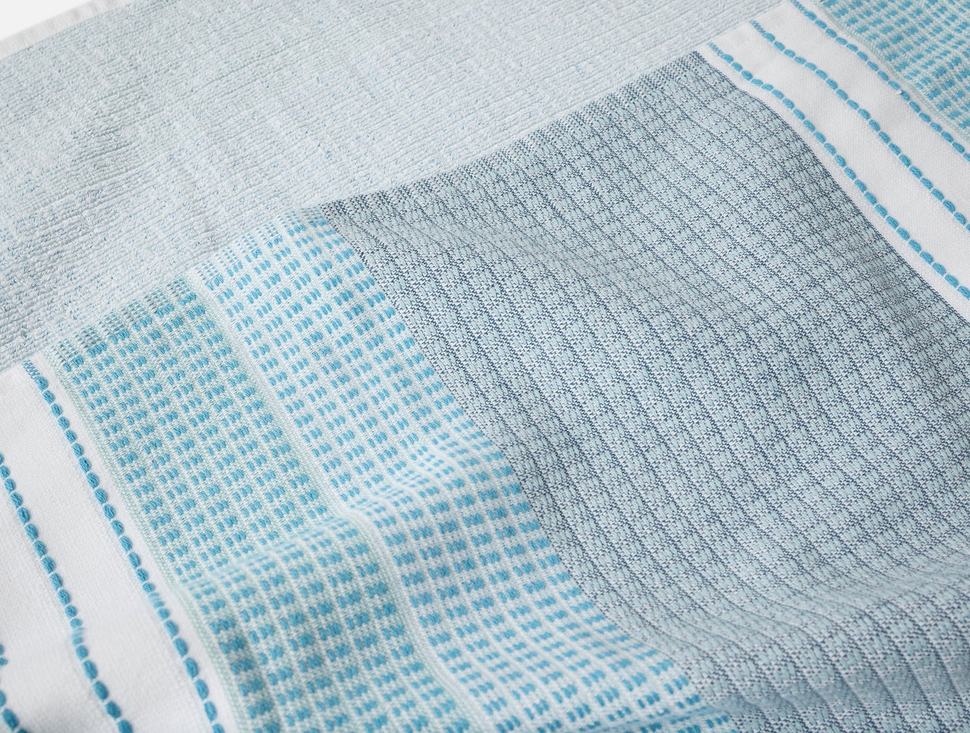 Close-up of Coyuchi Seabright beach towel showing aqua waffle weave texture and stripe detail.