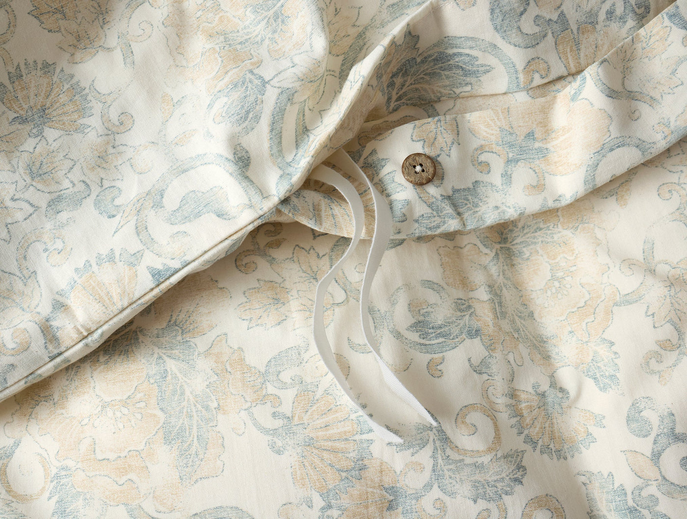 Close-up of Coyuchi Solana Print duvet cover button closure on ivory floral jacquard.