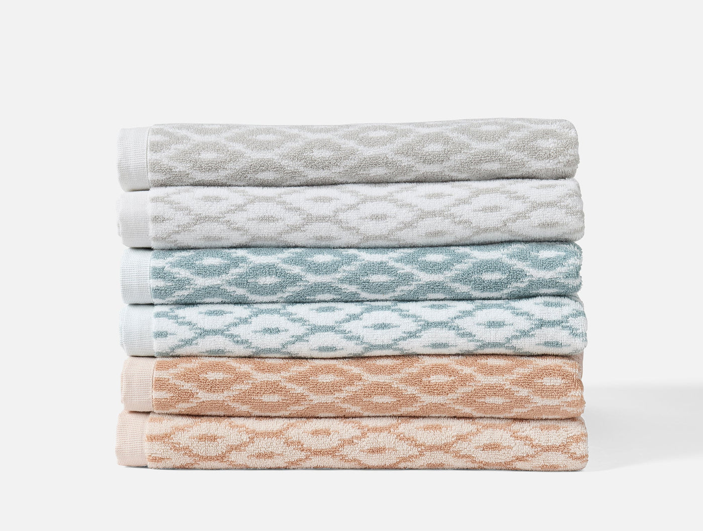 Stack of six folded Coyuchi Stinson bath towels in grey, aqua, and blush diamond jacquard.
