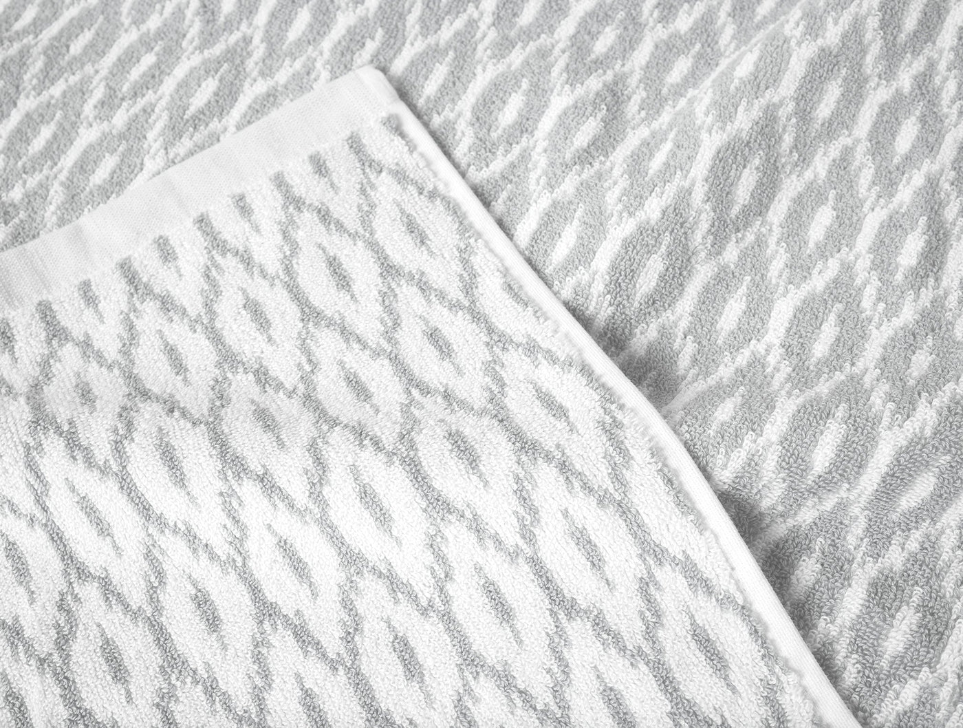Close-up of Coyuchi Stinson bath towel corner showing silver diamond jacquard weave on white.