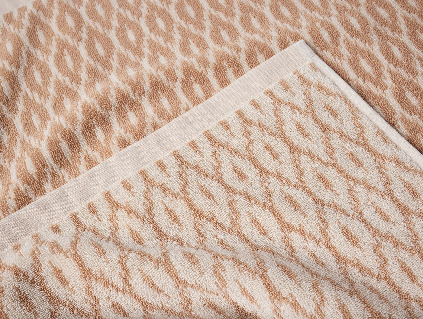 Close-up of Coyuchi Stinson bath towel showing camel diamond jacquard pattern and ivory border hem.