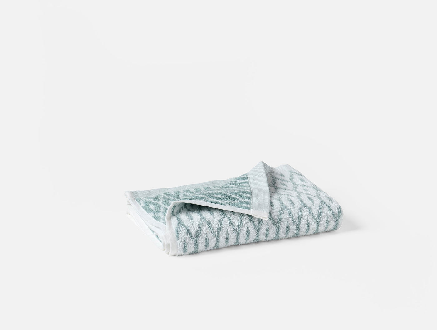 Folded sage and white ikat-pattern bath towel, reverse side visible at corner.