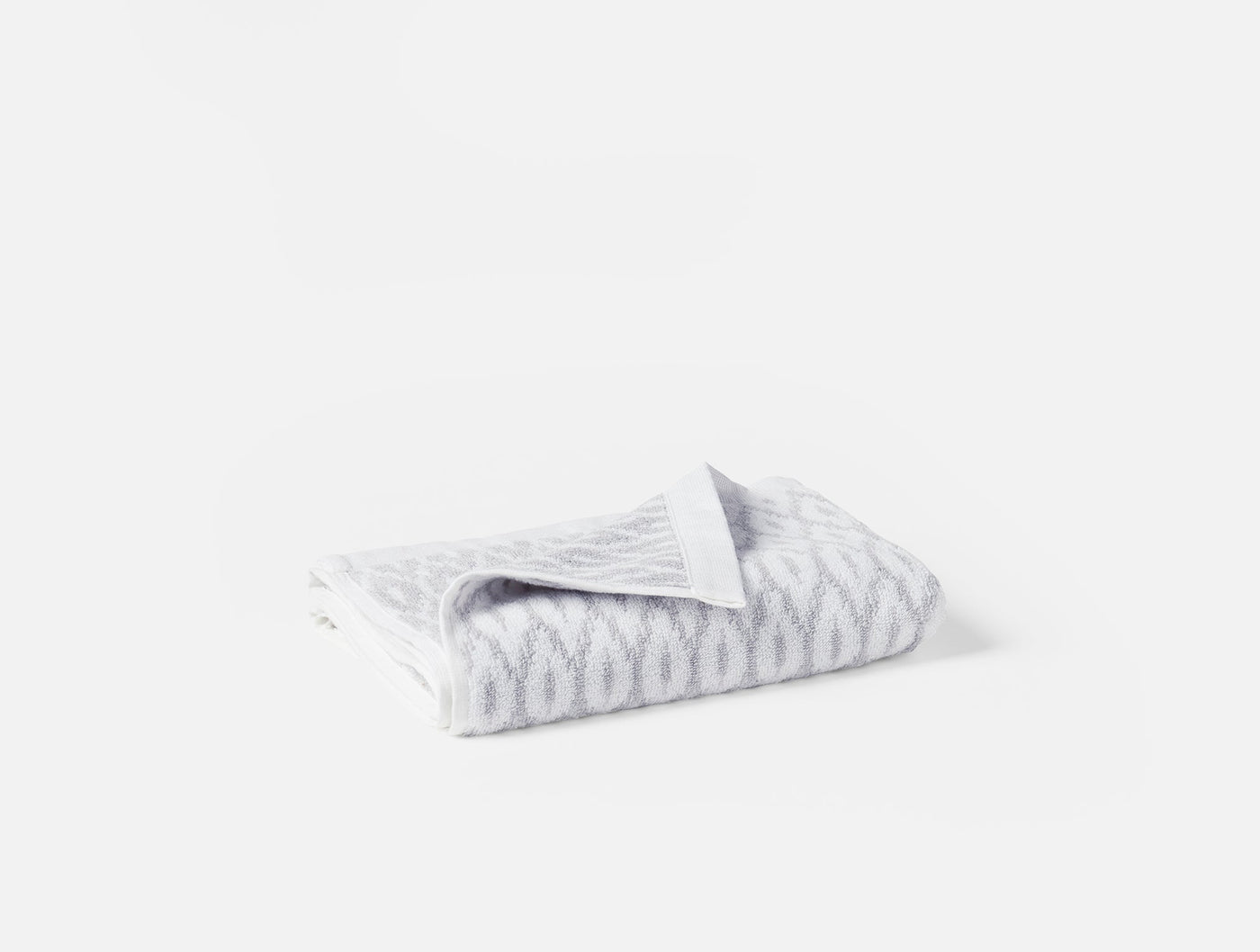 Folded Coyuchi Stinson bath towel showing silver-grey ikat chevron pattern on white ground.