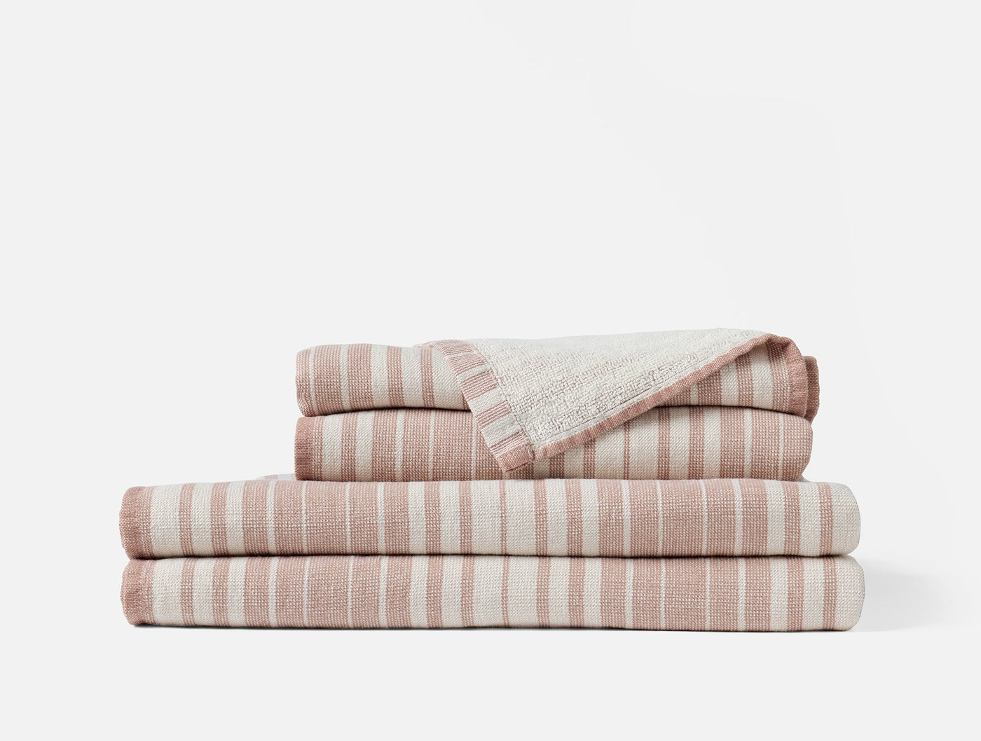 Folded stack of blush and ivory striped cotton linen towels, top towel corner turned back.