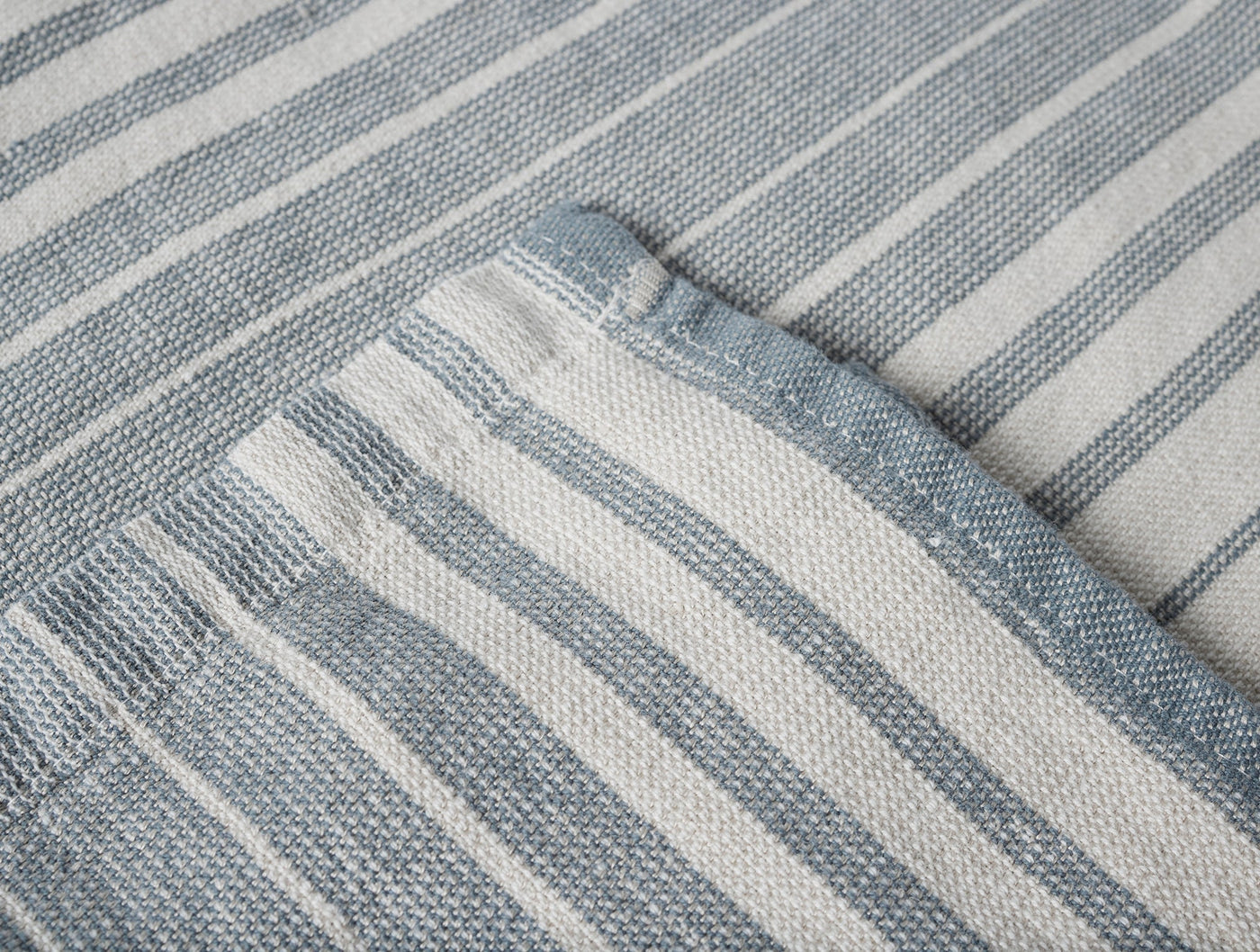 Close-up of Coyuchi Sycamore hand towel corner, slate blue and ivory ticking stripes, woven hem detail.