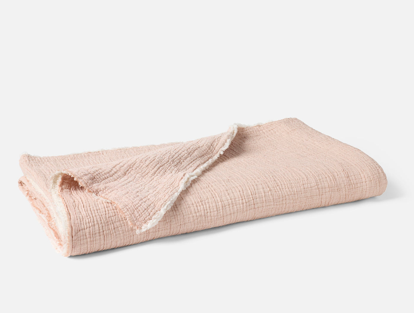 Folded blush matelassé blanket showing fringe edge detail against white background.