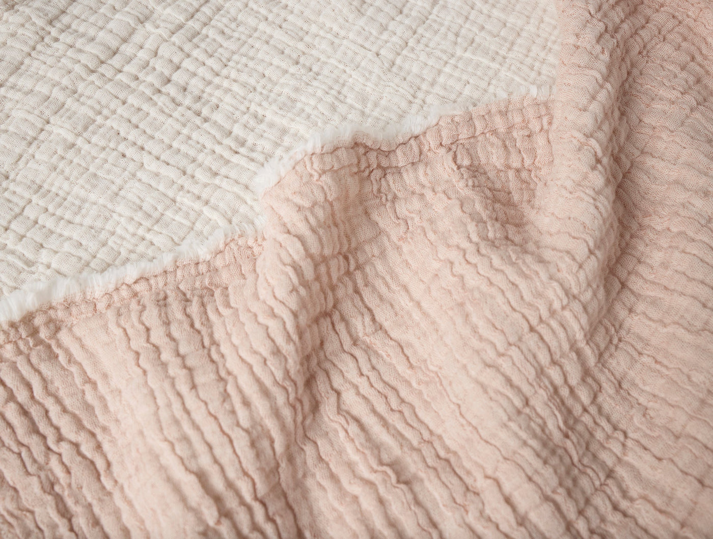 Close-up of blush and natural Coyuchi Topanga Matelasse blanket showing crinkled texture contrast.
