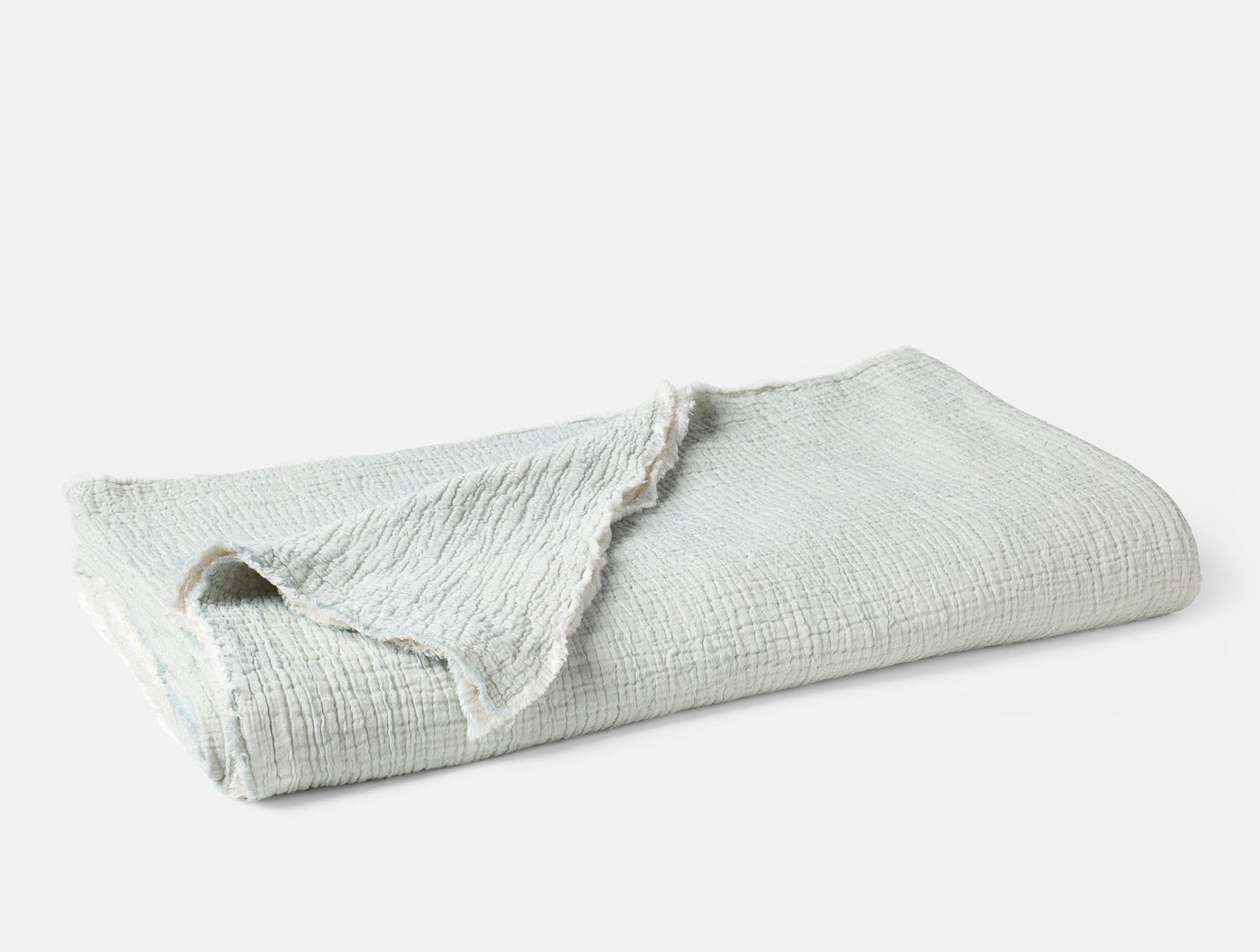 Folded ivory matelassé blanket with fringe trim, showing textured weave detail.