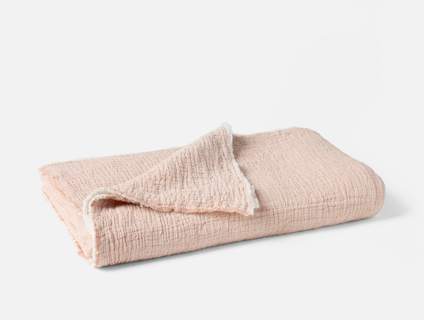 Folded blush Coyuchi Topanga Matelasse throw showing textured crinkle weave and soft edge detail.