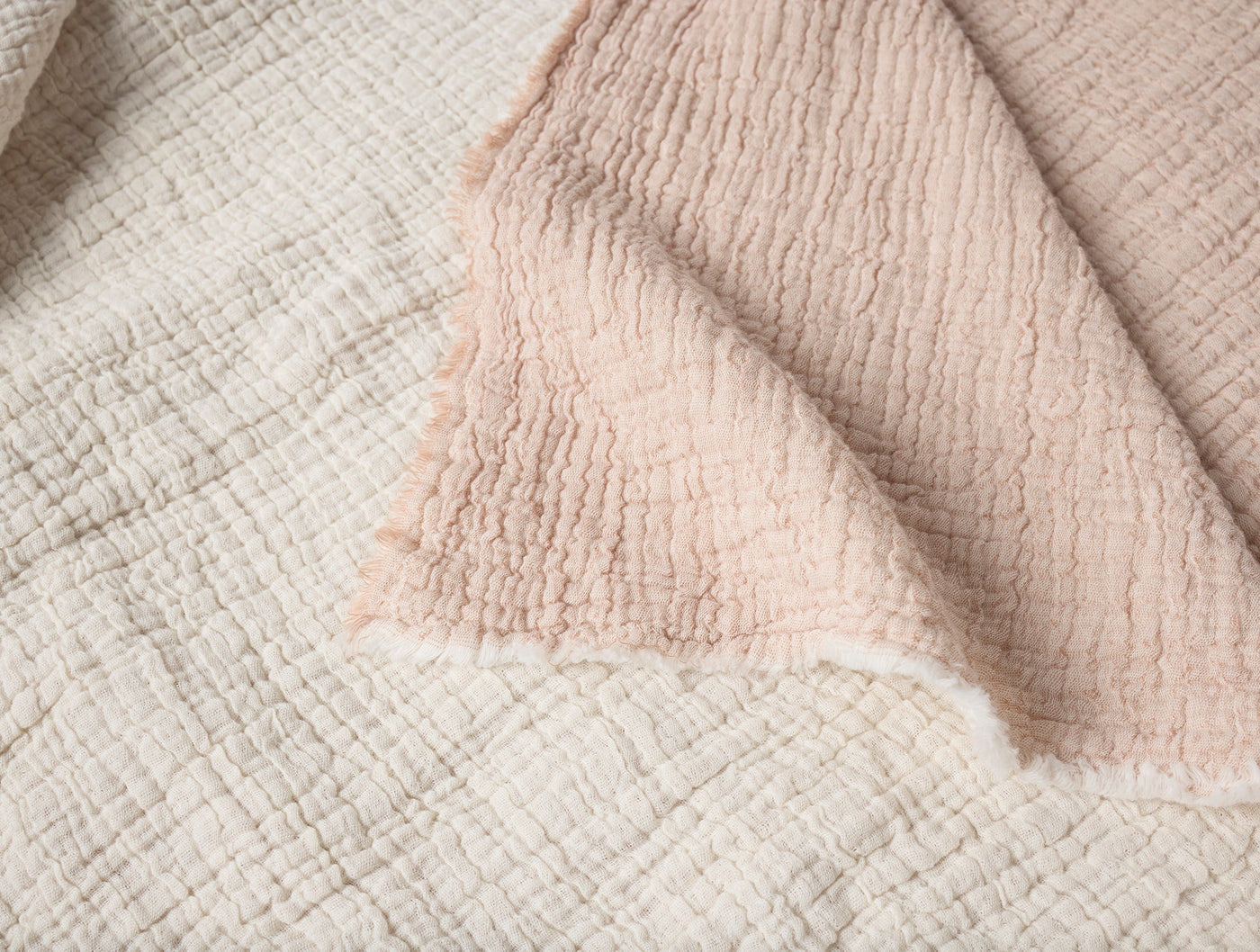 Close-up of Coyuchi Topanga Matelassé throw corner, ivory and blush reversible layers with frayed edge.