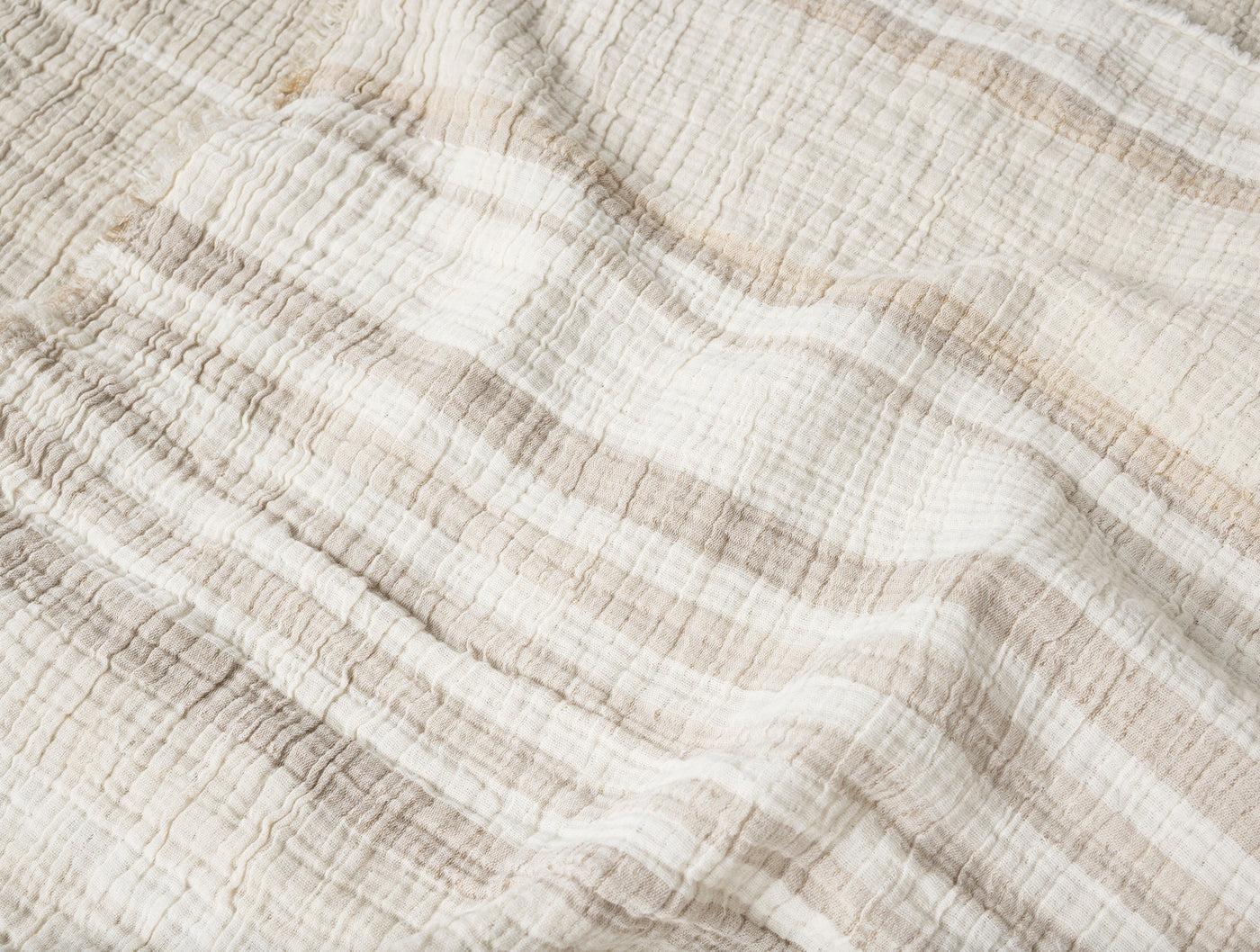 Close-up of ivory and sand striped matelasse throw, showing crinkled cotton texture.
