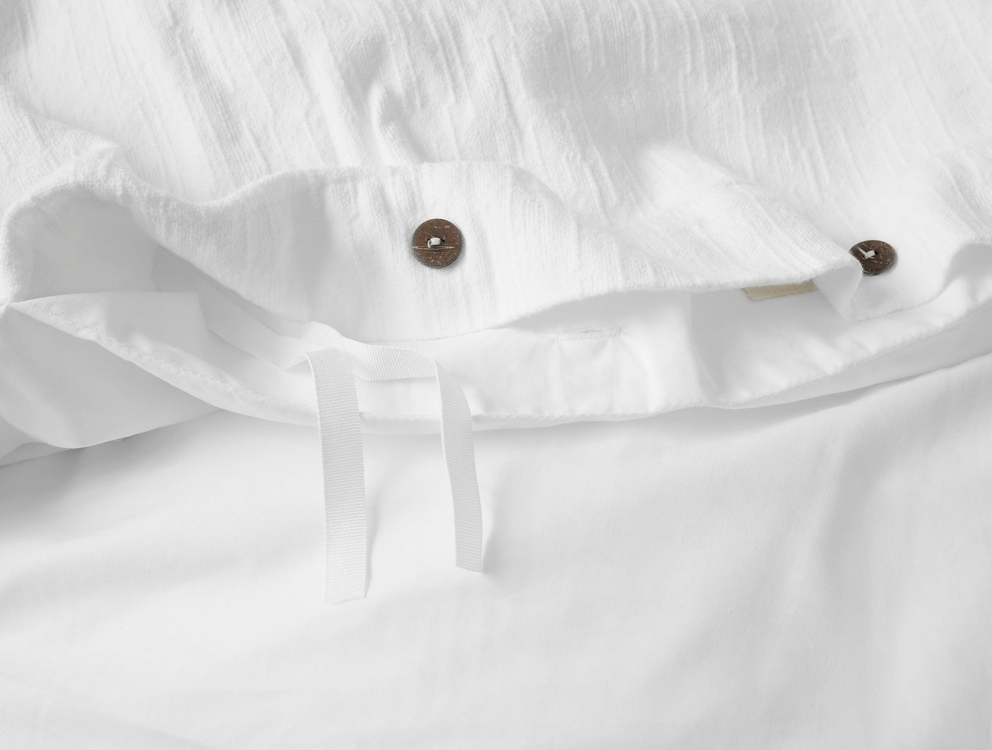 Close-up of white linen duvet cover closure with coconut shell buttons and interior ties.