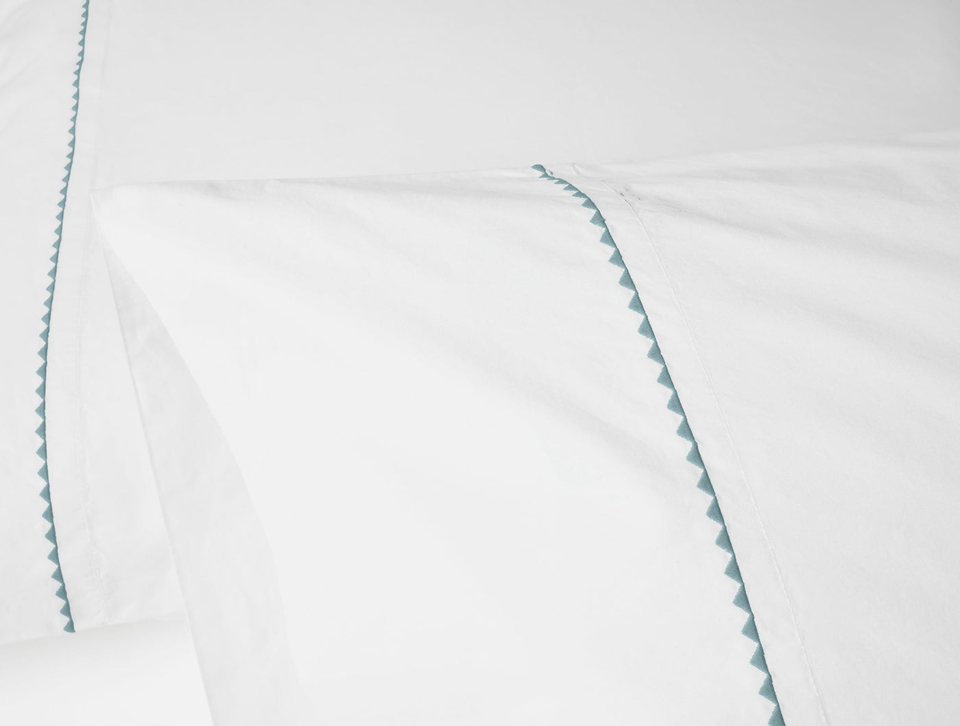 Close-up of teal zigzag embroidered hem detail on white Coyuchi pillowcase.
