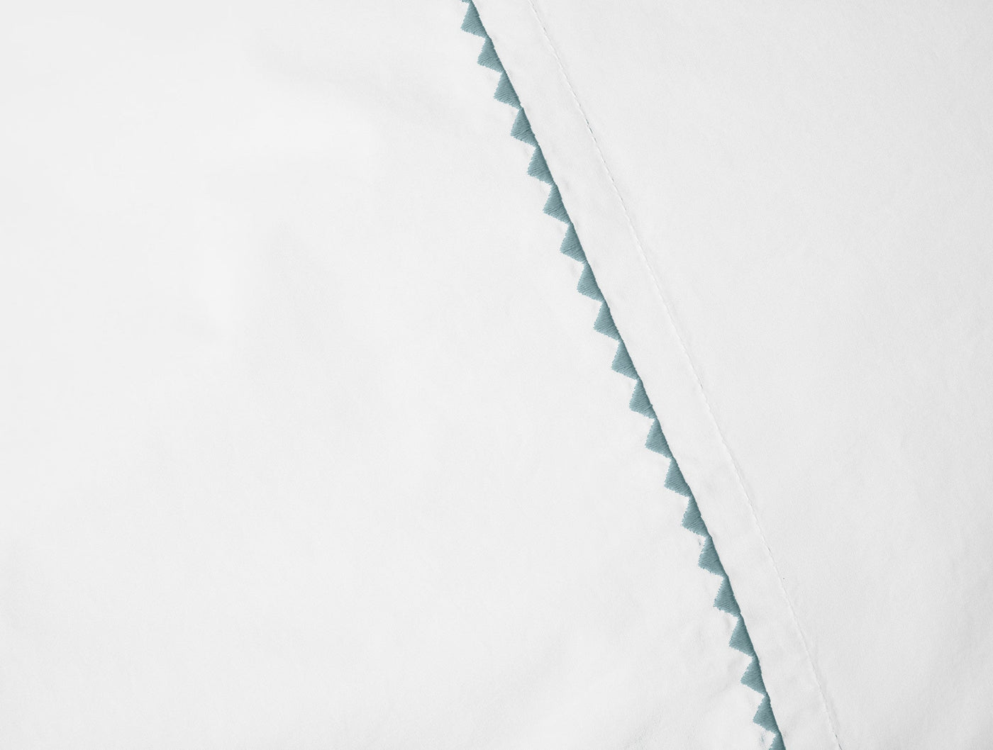 Close-up of white pillowcase hem with aqua zigzag embroidered trim detail.
