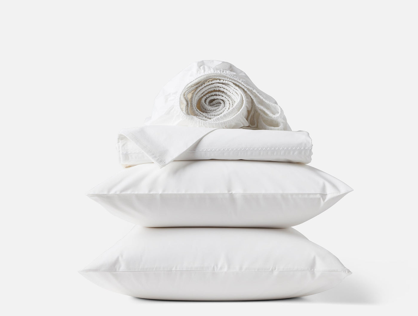 Coyuchi Trailing Embroidered sheet set in white, stacked with pillows and rolled linens.