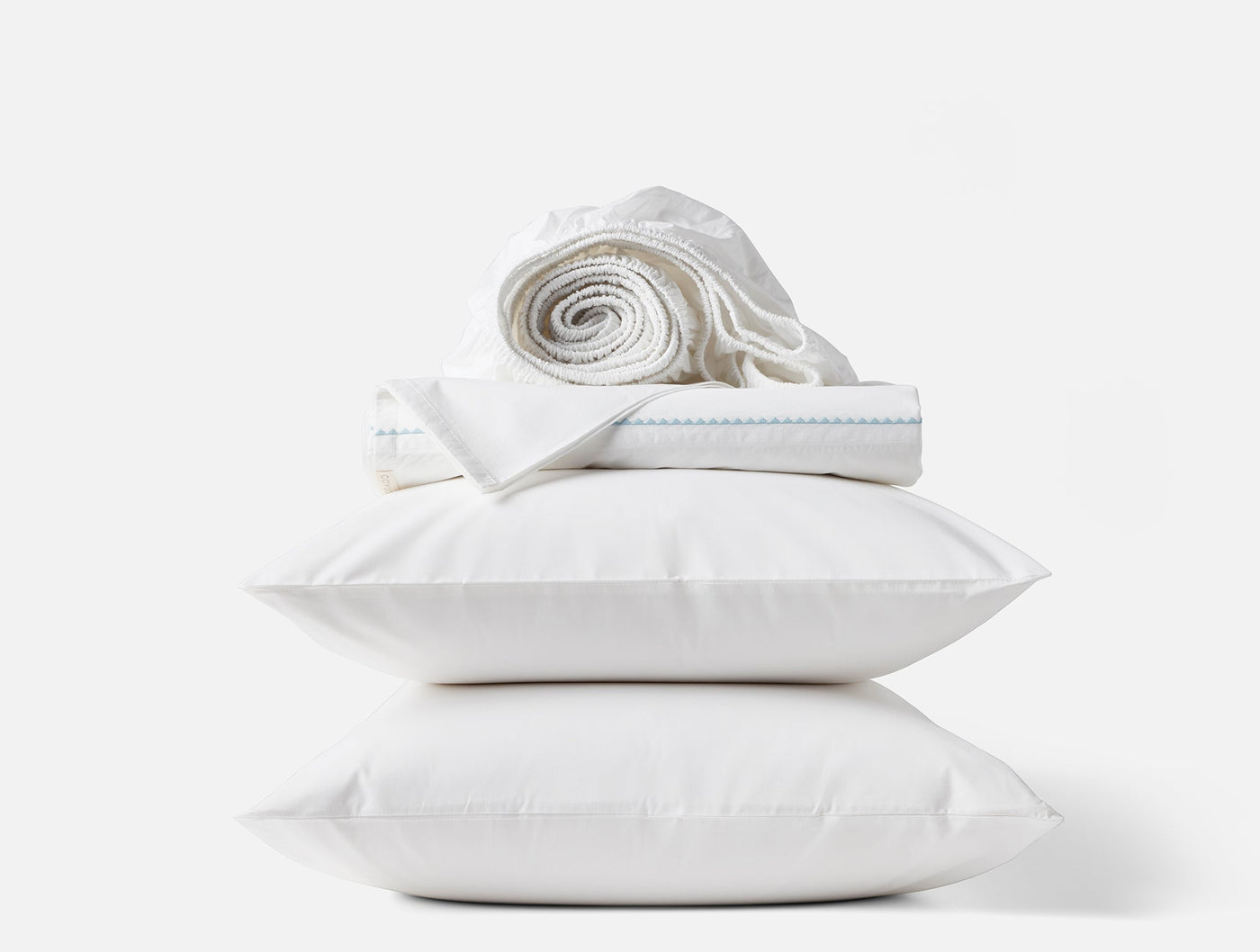 Close-up of two stacked white pillows with folded Coyuchi sheets and a rolled flat sheet on top.