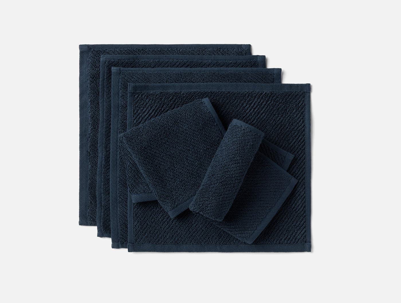 Six navy blue Coyuchi Air Weight washcloths stacked and folded on white background.
