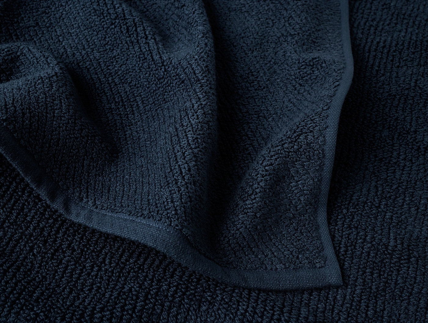 Close-up of Coyuchi Air Weight wash cloth corner in deep navy, showing terry texture and hem.