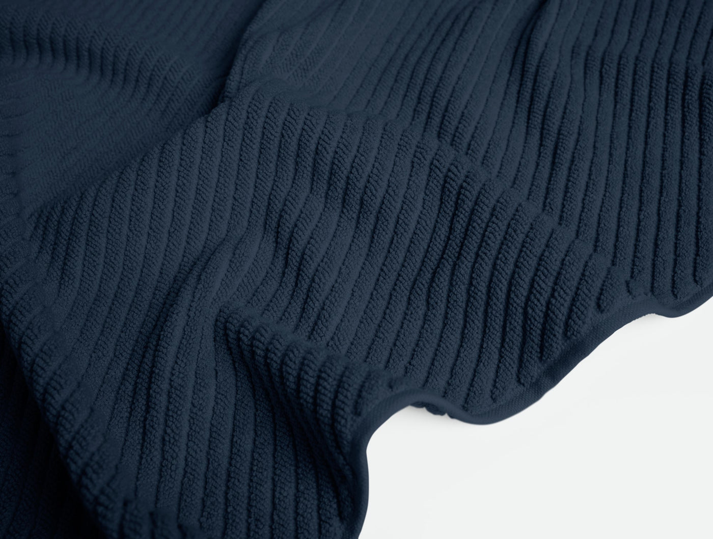 Close-up of draped navy Coyuchi Air Weight bath rug showing ribbed twill weave texture.