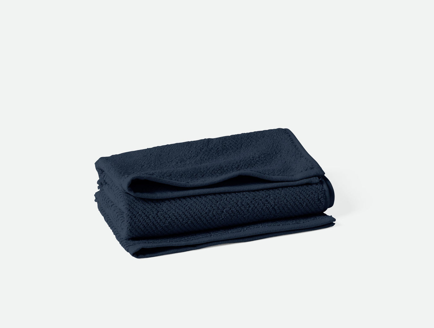 Folded navy Coyuchi Air Weight towel showing subtle woven texture, stacked on white background.