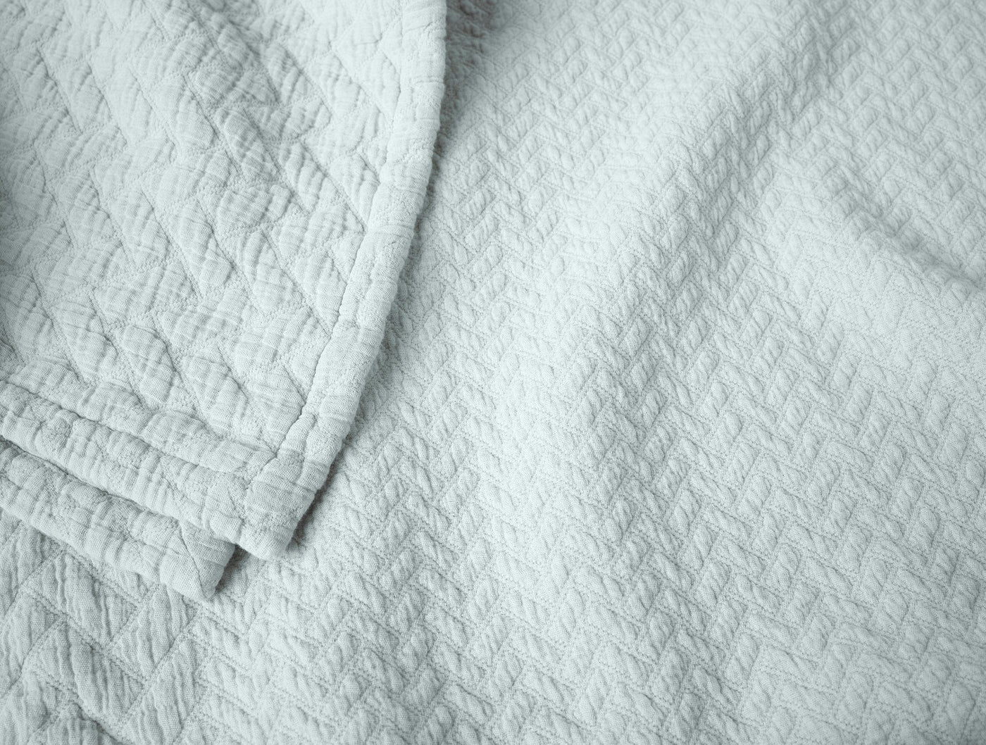 Close-up of Coyuchi Angeles Matelasse blanket in mist blue with subtle woven texture.