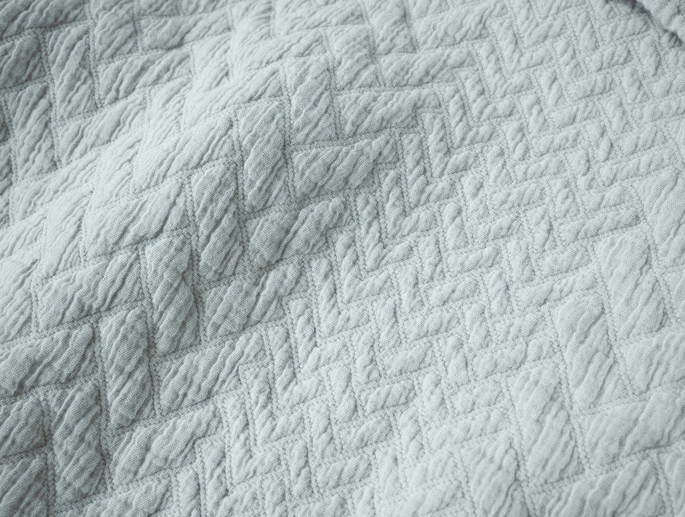 Close-up of Coyuchi Angeles Matelassé blanket in silver grey, showing quilted diamond weave texture.