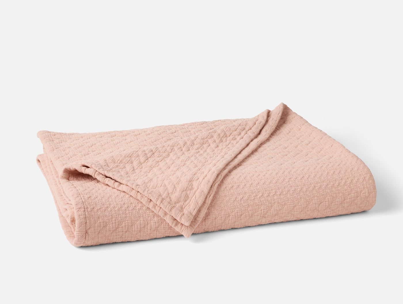 Coyuchi Angeles Matelassé blanket folded, showing blush cotton texture and diamond weave pattern.