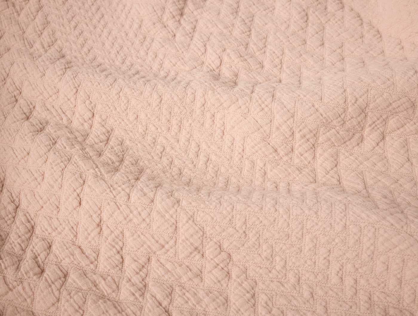 Close-up of Coyuchi Angeles Matelassé blanket in blush, showing quilted diamond weave texture.