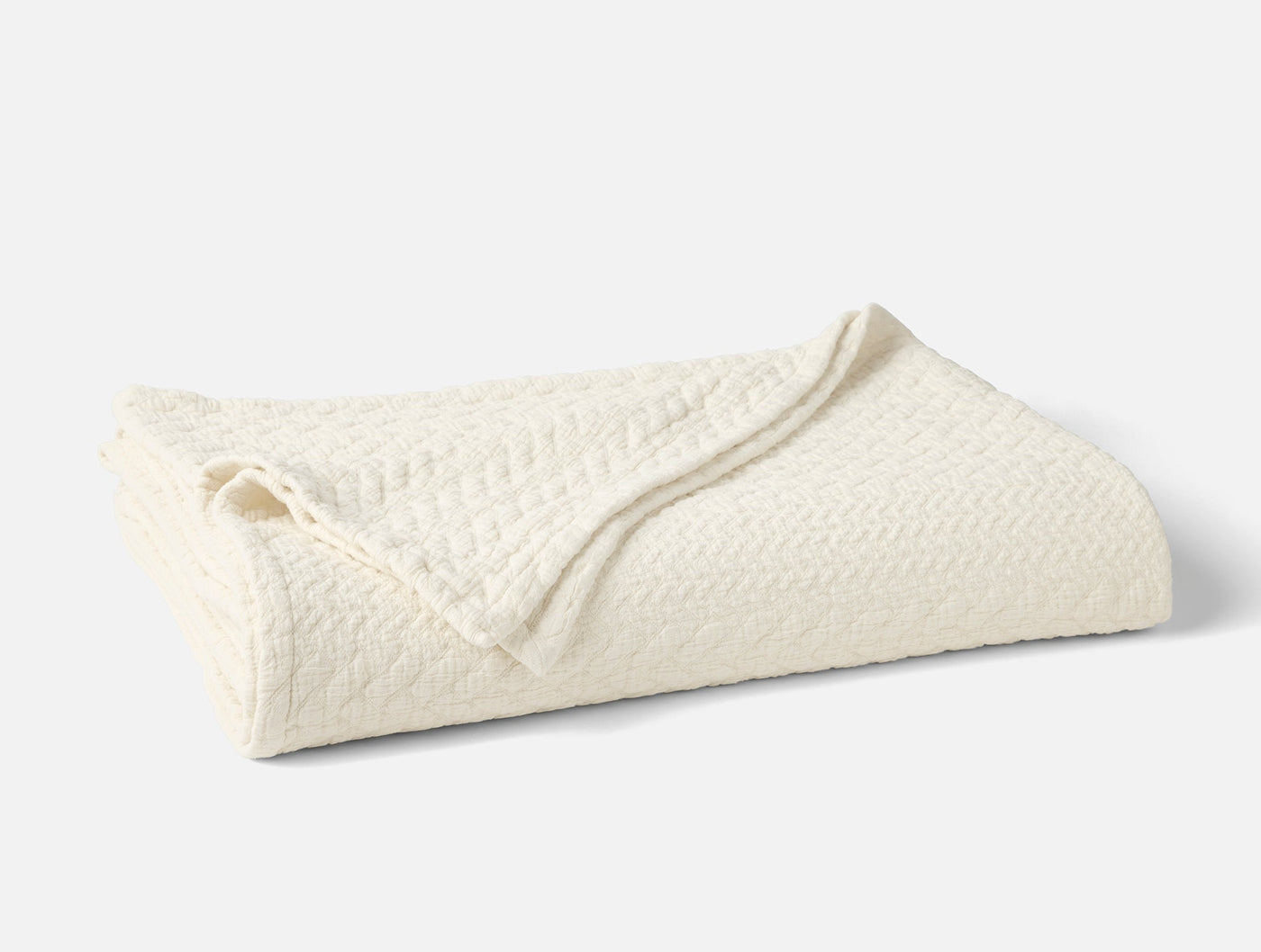Close-up of folded ivory Coyuchi Angeles Matelasse blanket showing textured weave detail.