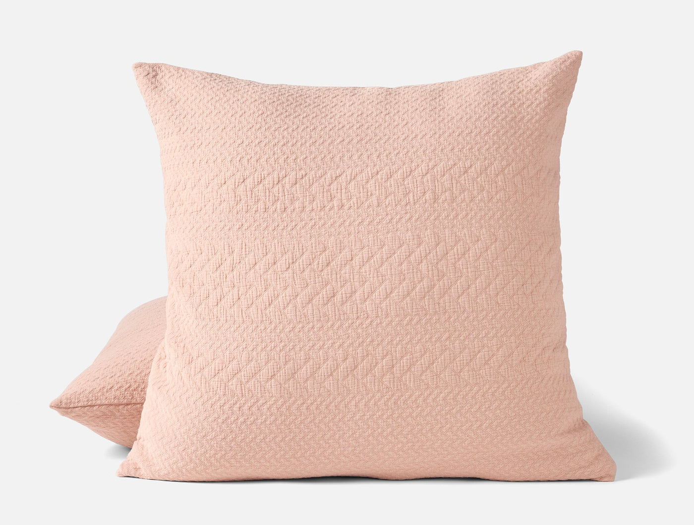 Blush pink matelassé pillow sham with subtle herringbone texture, shown front and side.