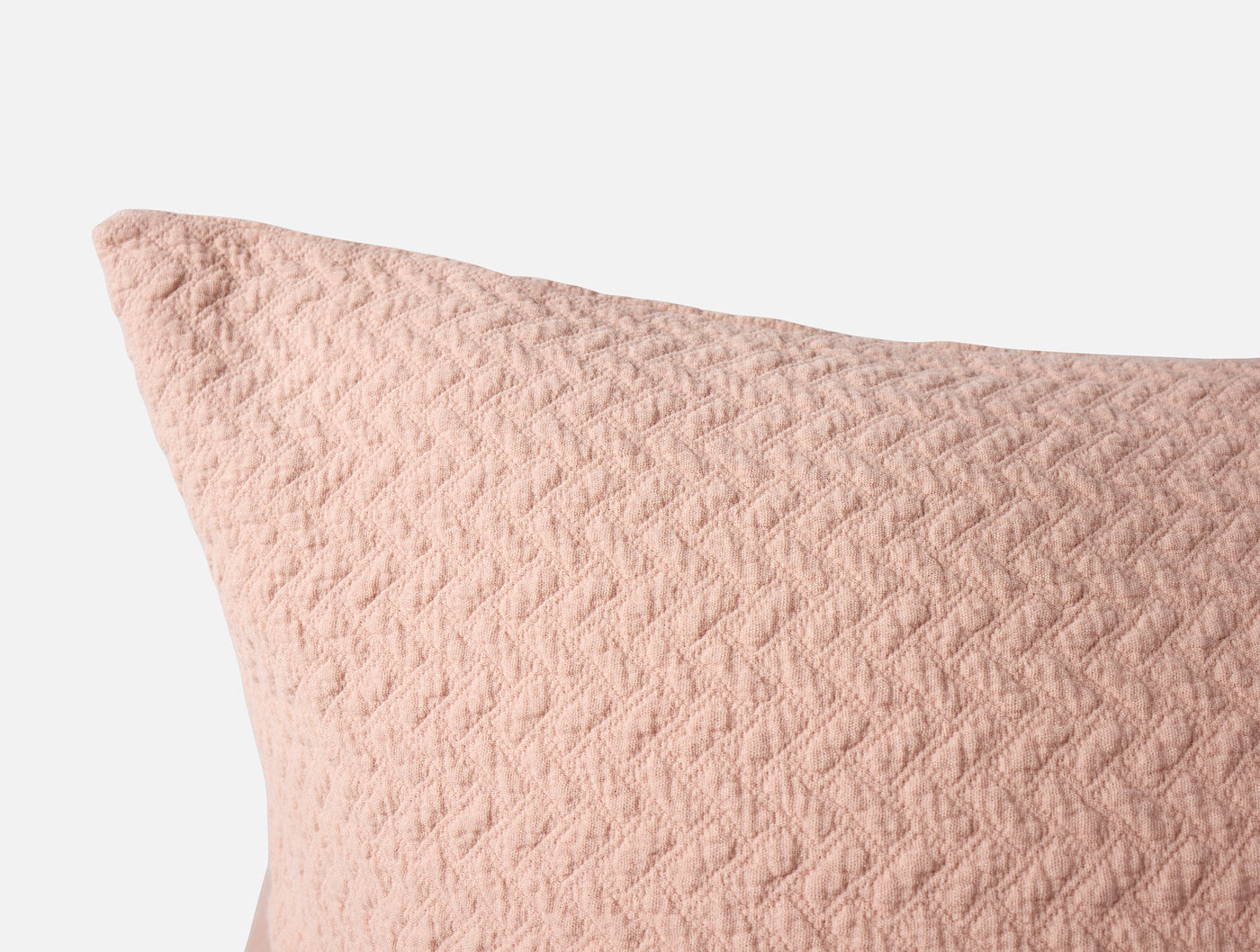 Close-up of blush Coyuchi Angeles Matelassé sham corner showing quilted diamond texture.
