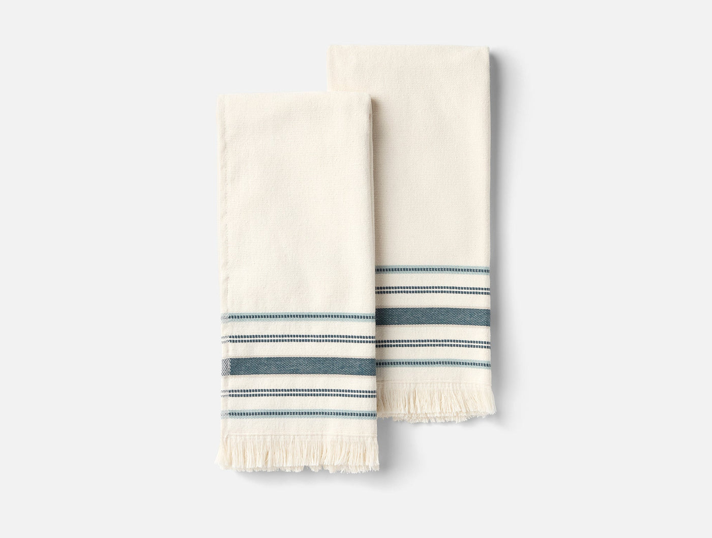 Close-up of two ivory Coyuchi Aptos hand towels with teal stripes and fringe hem.