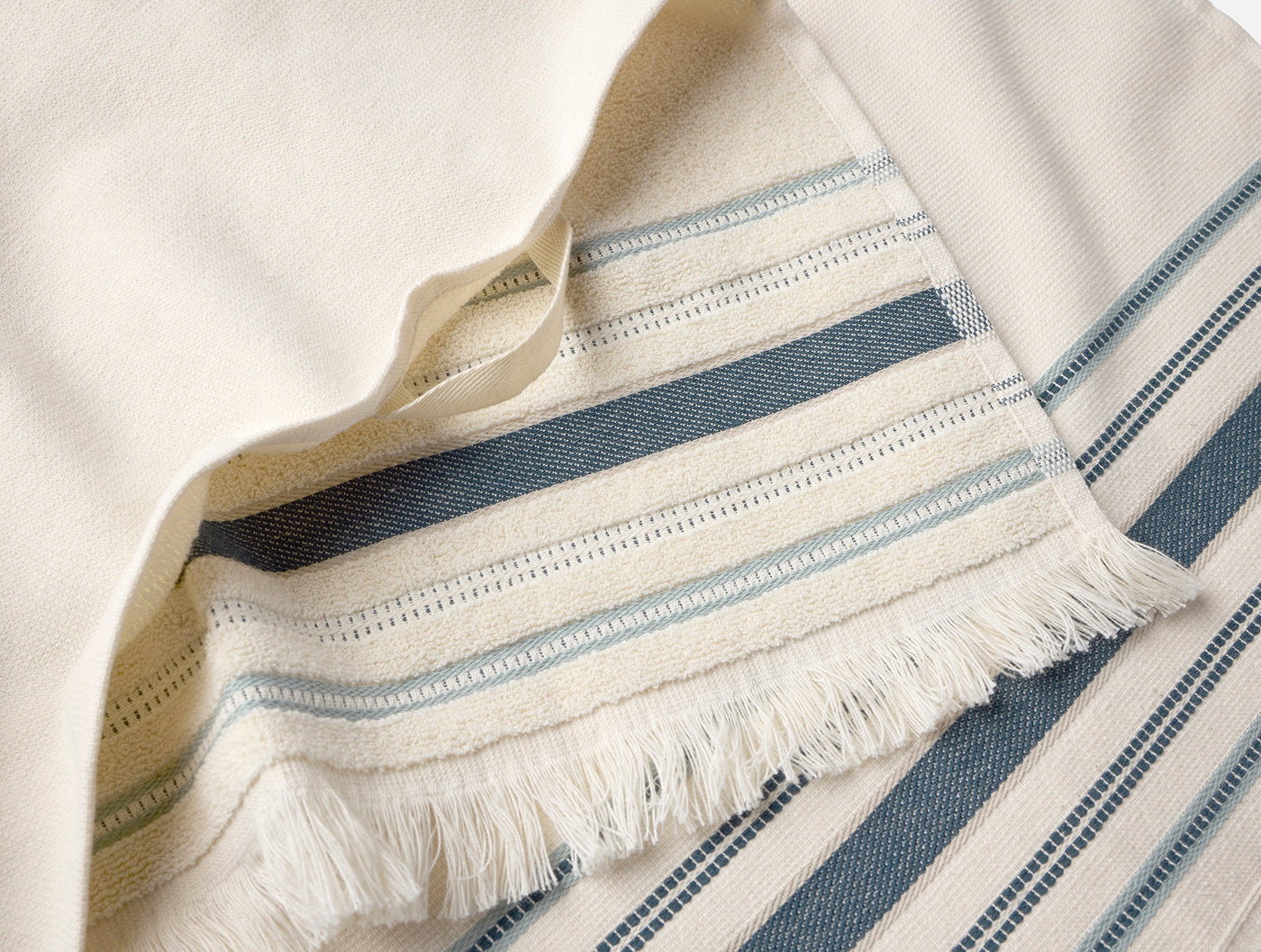 Close-up of Coyuchi Aptos hand towel hem with ivory fringe and slate blue woven stripes.